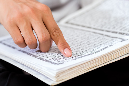 Asian Muslim man reading Koran or Quran on praying carpet wearing traditional dress