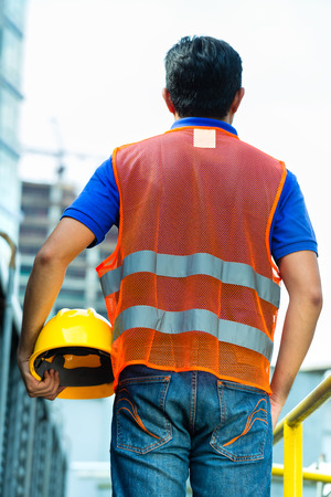 Asian Indonesian construction worker with helmet and safety vest on a building site in Asiaの写真素材
