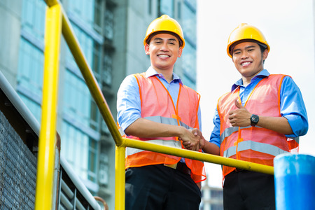 Asian Indonesian construction workers with blueprint or plan on building siteの写真素材