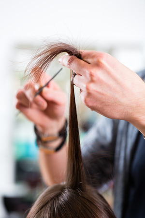 Male hairdresser cutting woman hair in hairdresser shopの写真素材