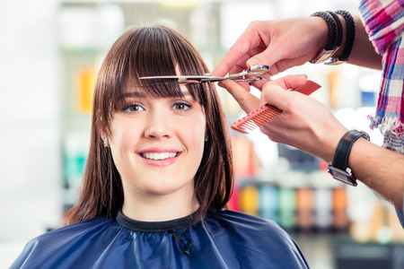 Hairdresser cutting woman bangs hair in shopの写真素材