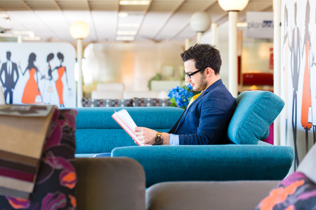 Young man reading hand-out and testing sofa in furniture storeの写真素材