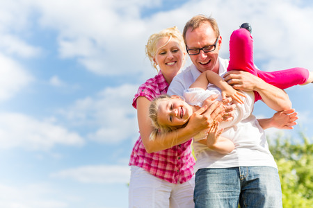 Family romping on field with parents carrying childの写真素材