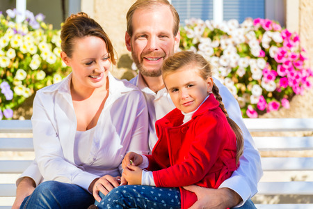 Family with mother, father and daughter together on garden bench in front of homeの写真素材