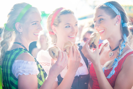 Friends visiting together Bavarian fair in national costume eating grilles sausage in bread rollの写真素材