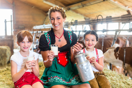 Bavarian mother sitting with children in cowhouse on hay bale drinking fresh milkの写真素材