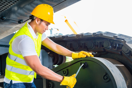 Asian motor mechanic working on construction or mining machinery in vehicle workshop