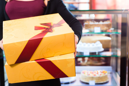 Woman presenting cake and pastries in takeaway boxes in cafe or pastry shopの写真素材