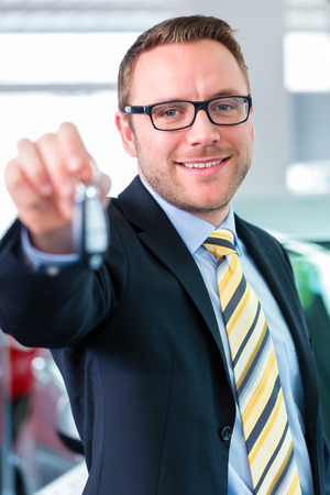 Salesman handing over auto key at car dealershipの写真素材