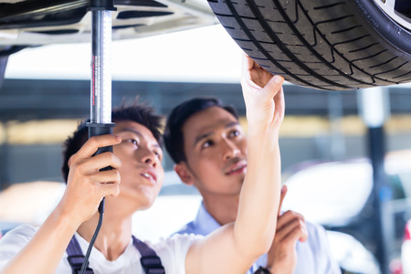 Asian Chinese car mechanic with customer looking at auto floor with lampの写真素材