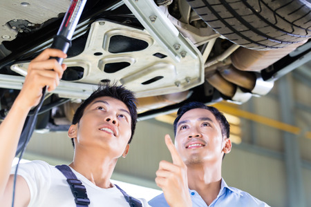 Asian Chinese car mechanic with customer looking at auto floor with lampの写真素材
