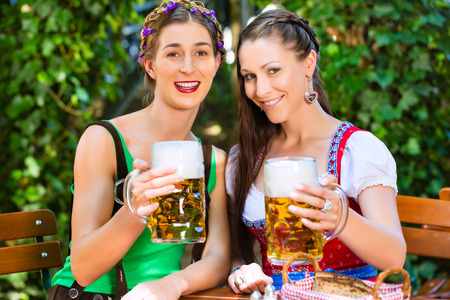 In Beer garden â female friends in Tracht, Dirndl and Lederhosen drinking a fresh beer in Bavaria, Germanyの写真素材