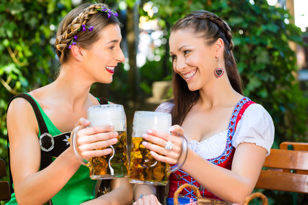 In Beer garden ? female friends in Tracht, Dirndl and Lederhosen drinking a fresh beer in Bavaria, Germanyの写真素材