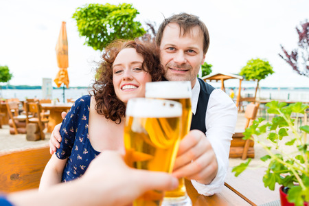 couple toasting toward friends in beer garden pubの写真素材