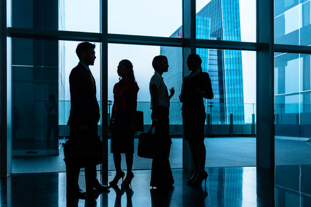 Group of business people standing in lobby or hall, a city skyline in the background, silhouette shotの写真素材