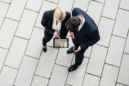 Business man and woman  with tablet computer standing on square, seen in top viewの写真素材