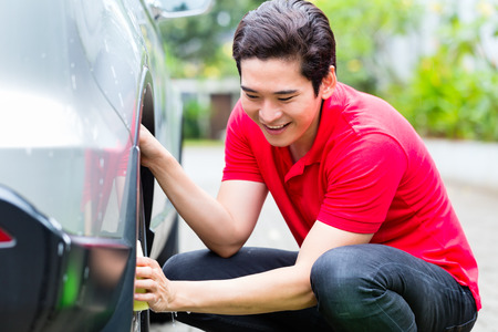 Asian man cleaning car rims with spongeの写真素材