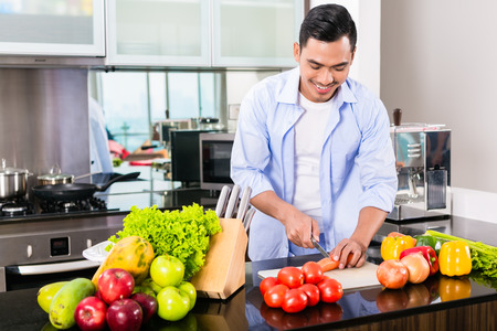 Asian man cutting vegetables in domestic kitchen preparing saladの写真素材