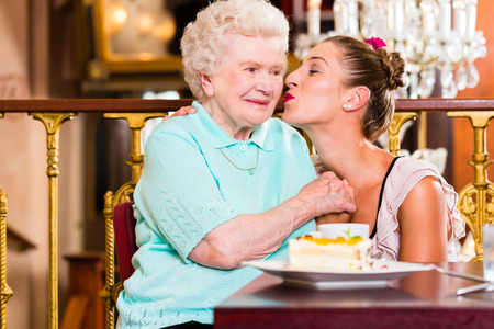 Senior woman and granddaughter with cake in old fashioned cafeの写真素材