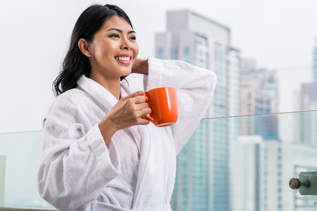 Asian woman in morning front of city skyline drinking coffeeの写真素材