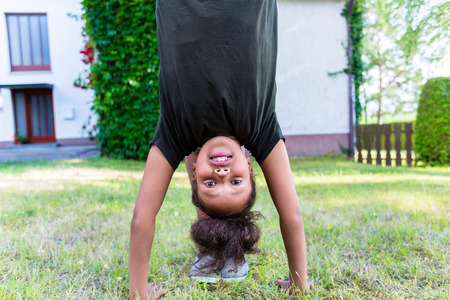 African girl playing on meadow in front of home doing handstandの写真素材