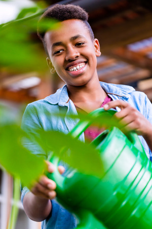 Young African boy watering plants in garden with canの写真素材