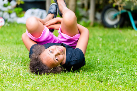 African girl playing on meadow in front of picket fence rolling around