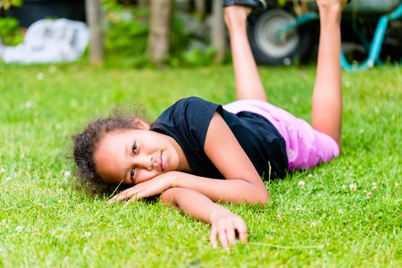African girl playing on meadow in front of picket fence rolling aroundの写真素材
