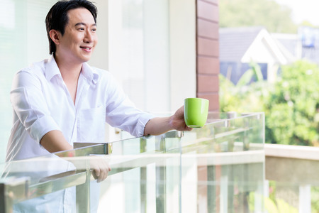 Chinese man on balcony of home with coffee in the morningの写真素材