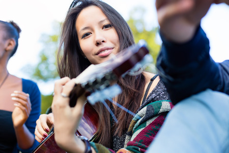 Guitar player Asian girl making music with friends in parkの写真素材