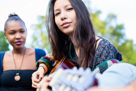 Guitar player Asian girl making music with friends in parkの写真素材