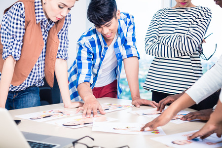 Advertising agency team choosing model for campaign among pictures spread out on tableの写真素材