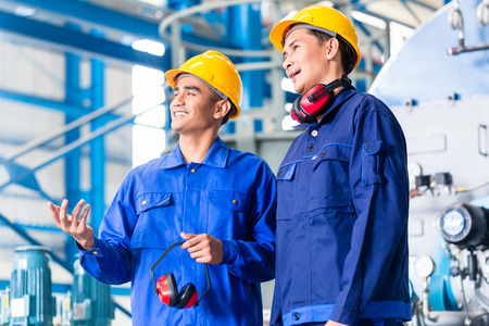 Worker in Asian manufacturing plant discussing in front of machinesの写真素材