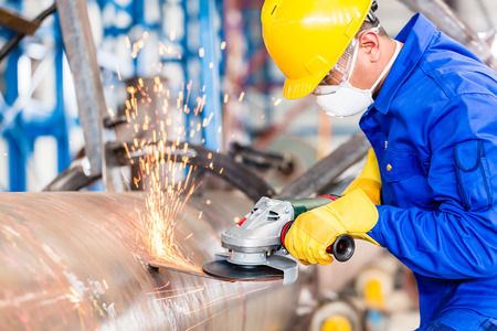 Industrial worker in manufacturing plant grinding to finish a pipeline