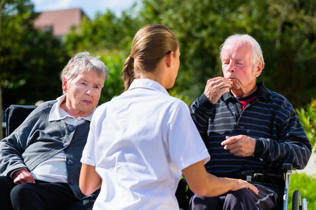 Seniors, couple of man and woman sitting in wheelchair, eating candy in garden of nursing home