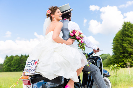 Wedding groom and bride driving motor scooter having fun, a just married sign attachedの写真素材