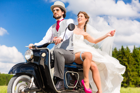 Wedding concept, bride and groom on motor scooter, she is showing her garter on legの写真素材
