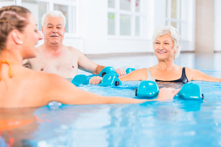 People young and senior in water gymnastics physiotherapy with dumbbellsの写真素材