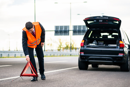 Man with car breakdown erecting warning triangle on roadの写真素材