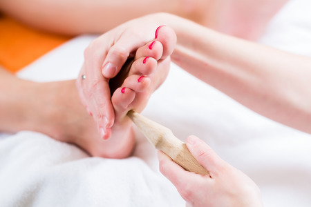 Women at reflexology having foot massaged or pressed with wooden stickの写真素材
