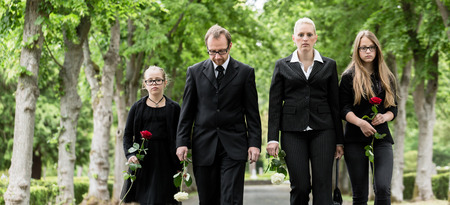 Family on cemetery walking down alley at graveyard with roses