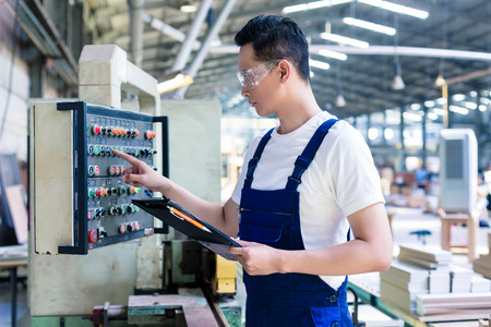 Worker pressing buttons on CNC machine control board in Asian factoryの写真素材