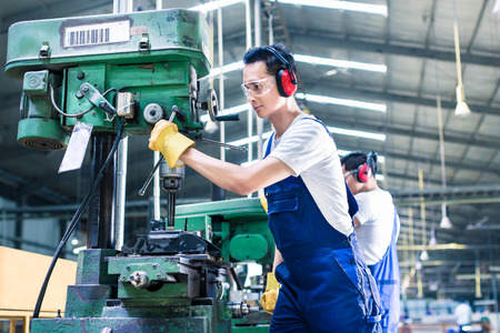 Asian worker in production plant drilling at machine on the factory floor Asian worker in production plant drilling at machine on the factory floor