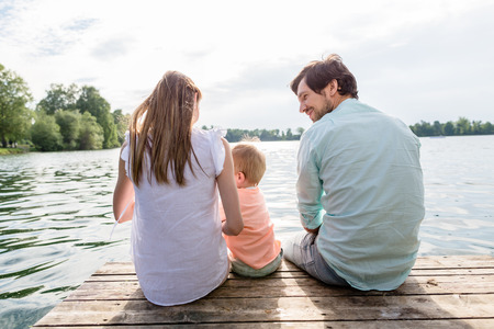 Family sitting on jetty of pond or lake in summerの写真素材