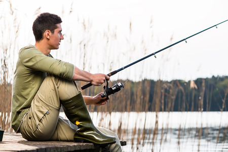 Man relaxing fishing or angling at lake sitting cross-legged on jettyの写真素材