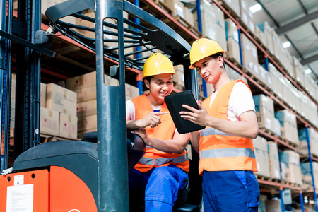 Workers in logistics warehouse at forklift checking list Workers in logistics warehouse at forklift checking list