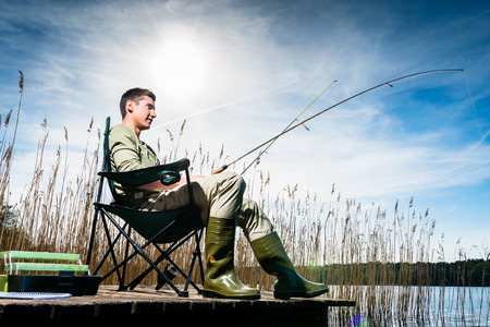 Man fishing at lake sitting on jetty close to the waterの写真素材