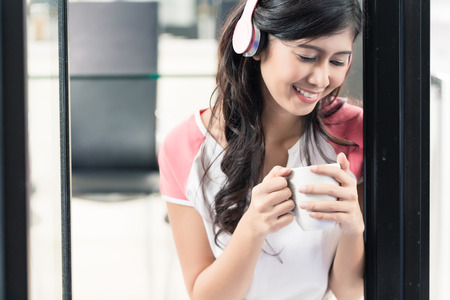 Indonesian woman listening to music with headphones at home with coffeeの写真素材