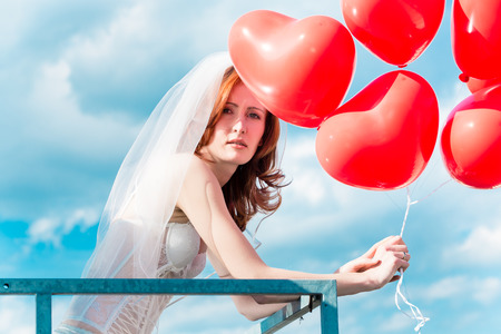 Bride with red balloons on balcony in lingerieの写真素材