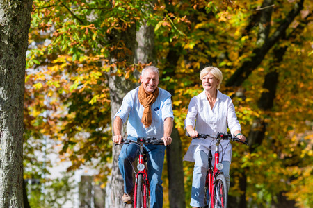 Senior couple, man and woman, on bicycles having bike tour in autumn parkの写真素材